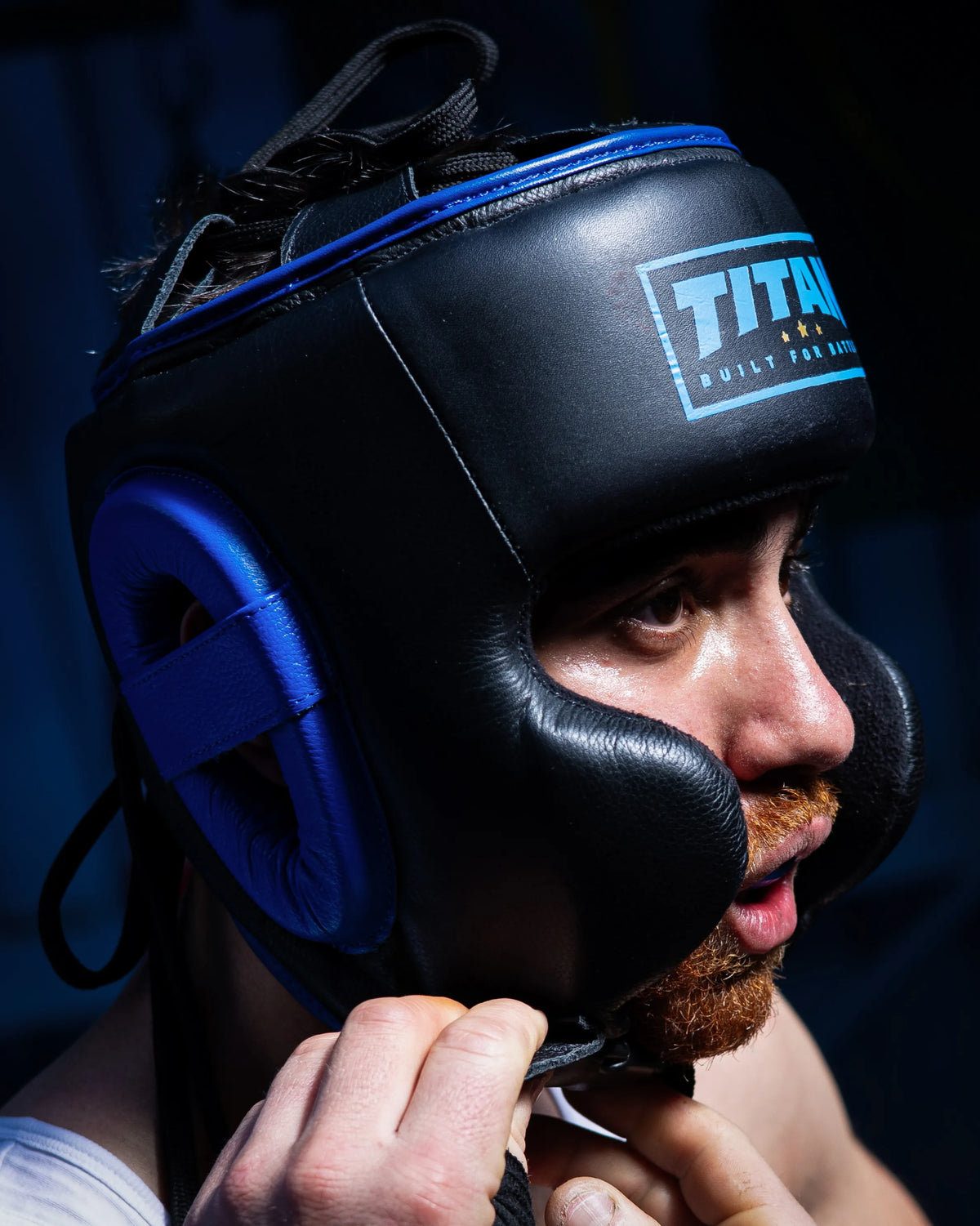 Boxer fastening a custom black Titan headguard with blue trim and Built For Battle logo