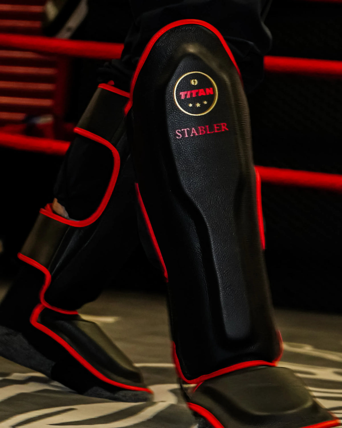 Personalised black Muay Thai shin guards with red piping and STABLER lettering, ringside