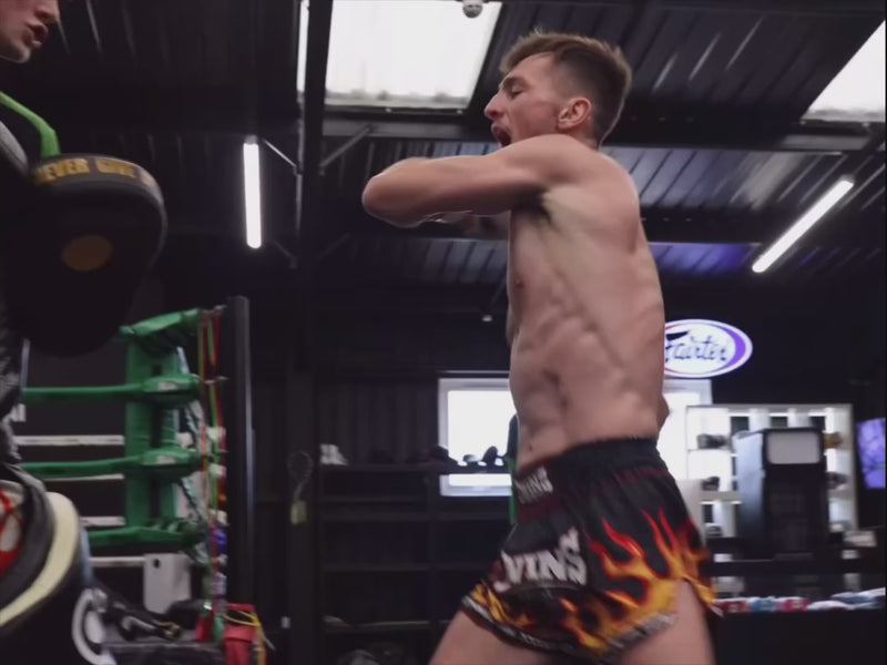 Muay Thai fighter in flame shorts throwing a kick at pads