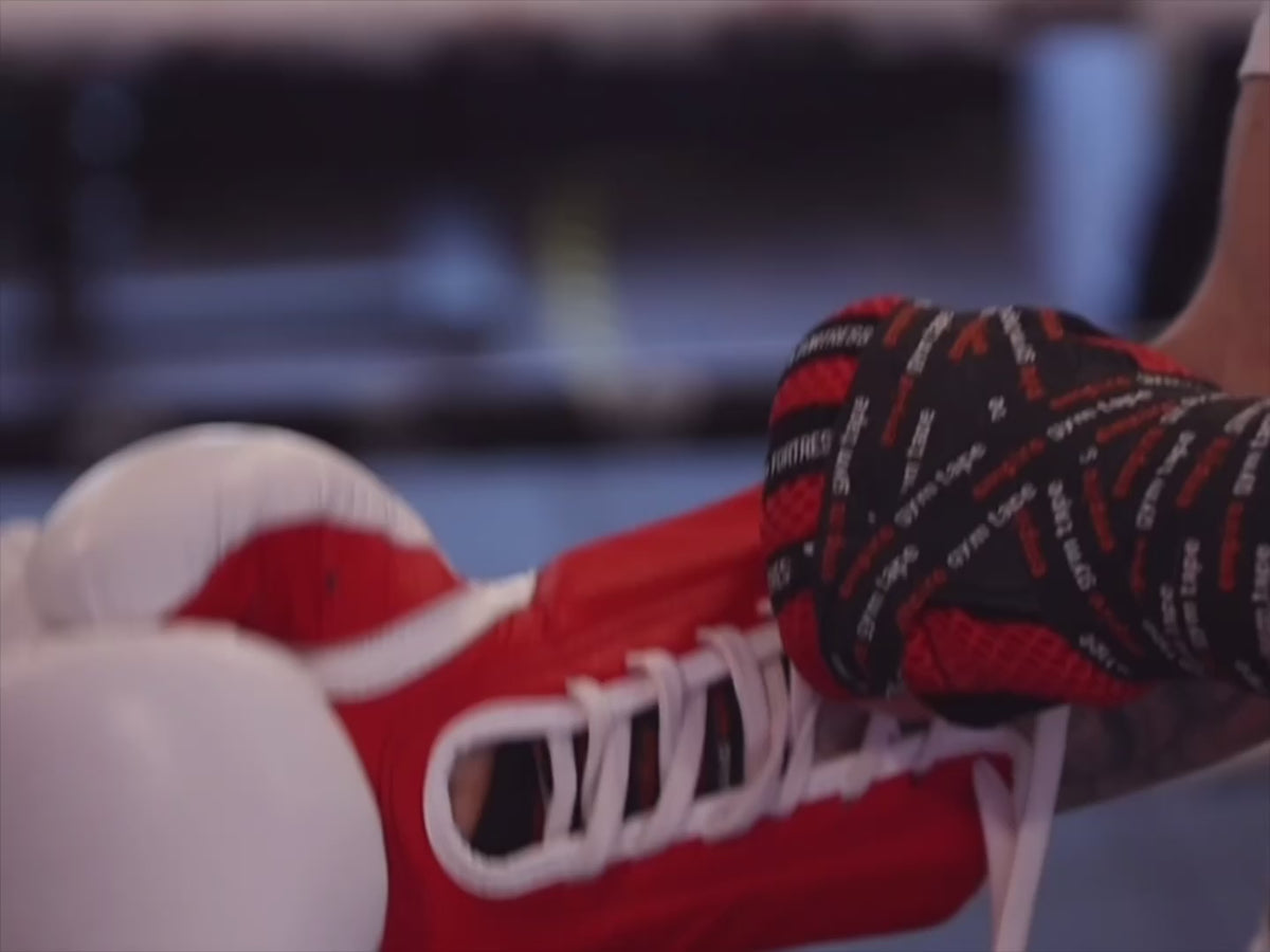 Load video: Close-up of red lace-up boxing gloves being tied